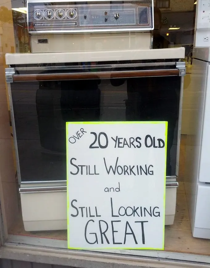A used-appliance store window sign reading over 20 years old, still working, still looking great, beside an old electric range